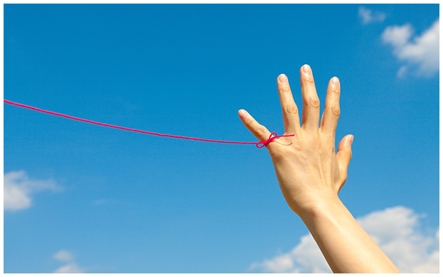 写真：青い空を背景に赤い糸が小指に結ばれた手